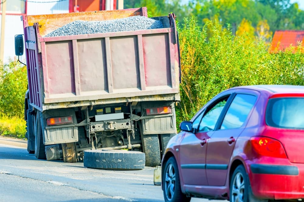A truck loaded with gravel sits by the roadside, its damaged wheel hub and tire evidence of an accident. It awaits maintenance, stranded until repairs can be made.